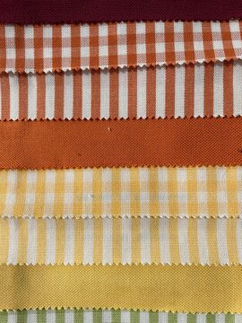 Collection of orange and yellow fabric swatches featuring checkered, striped, and solid patterns stacked in rows 