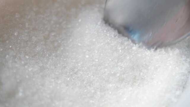 Macro shot of silver spoon scooping white granulated sugar from bowl