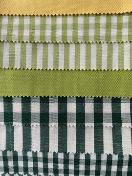 Collection of fabric samples featuring various green, white, and dark checkered, striped, and solid patterns arranged in rows 