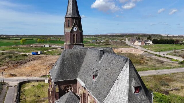 drone rises past slate church roof revealing brick bell tower clock face manheim alt demolished village cleared land surrounds kerpen germany north rhine westphalia farmland stretches horizon