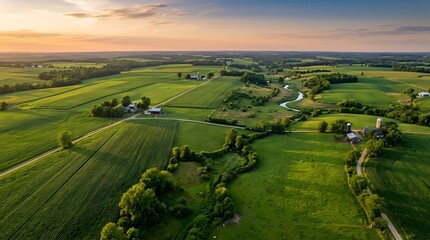 Obraz premium An expansive aerial perspective captures vibrant green agricultural fields a meandering river and rural farm structures bathed in the warm glow of a setting sun across rolling countryside terrain