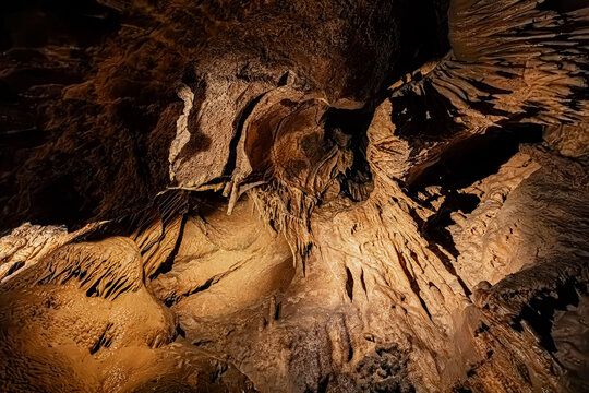 Cascade of mineral formations and wall draperies beneath a high rocky ceiling in a cave, Pyrenees, France