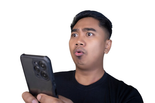 Surprised and startled Indonesian man in a black t-shirt looking at his smartphone with a rounded open mouth and wide eyes against a white background.