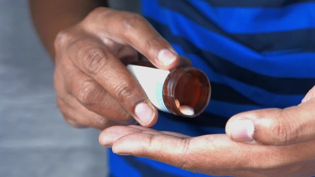Close up shot of person hands pouring out white pills from bottle into palm showing medical concept and medication dosage