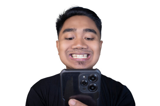 Awkward and uneasy Indonesian man in a black t-shirt looking down at his smartphone with a tight-lipped smile and cringing expression against a white background.