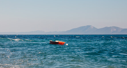 Small red boat floating on clear blue ocean water with distant mountains visible under a bright sky in a serene coastal landscape © Надія Коваль