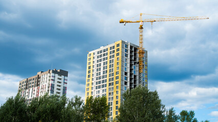 Tower crane working on the construction of a modern residential high-rise building against a cloudy blue sky, urban development © Oleksandr Baranov