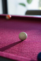 Fototapeta premium White cue ball is resting on red felt pool table, casting long shadow toward lower-left