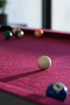 White cue ball sitting sharp on burgundy felt pool table near vertical window, blurred balls
