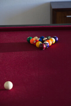 Triangular rack of colorful billiard balls sitting on maroon pool table near wall, cue ball resting