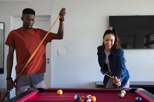 Diverse couple playing pool in home game room on red-felt table with cues and balls