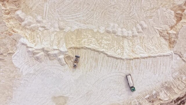 Two trucks are at a construction site moving materials on rough terrain. The site has been cleared and prepared for work. Dust is present in the area as machines operate.