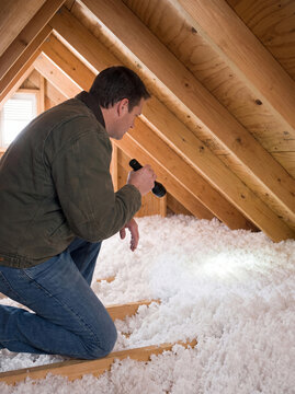 Homeowner inspecting attic insulation with flashlight