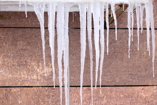 Long icicles hanging from a roof edge against a plain exterior wall in winter, illustrating freezing temperatures, cold weather, ice formation, and winter hazards.