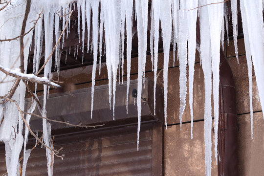 Long icicles hanging from a roof edge against a plain exterior wall in winter, illustrating freezing temperatures, cold weather, ice formation, and winter hazards.