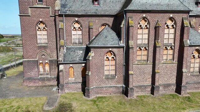 boarded gothic windows brick apse church wall close aerial pass isolated manheim alt kerpen germany plywood covered glass empty grass surrounds no buildings nearby deconsecrated parish