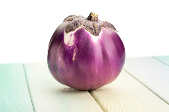 round purple eggplant on wood background on white