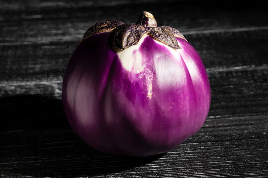 round purple eggplant on black wood background
