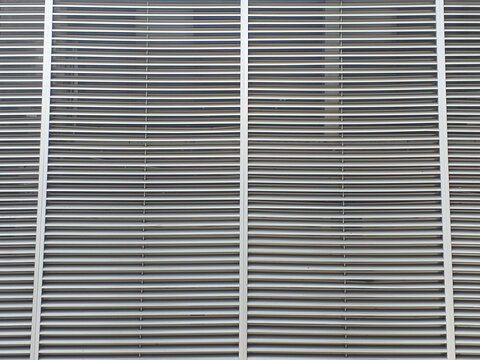 Close‑up of metallic vent grille with parallel horizontal slats divided by vertical bars. The repetitive pattern and curved design highlight industrial symmetry and architectural precision.  