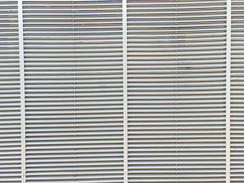 Close‑up of metallic vent grille with parallel horizontal slats divided by vertical bars. The repetitive pattern and curved design highlight industrial symmetry and architectural detail. 