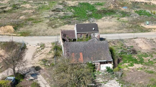 ivy covered farmhouse decays beside empty country road collapsed roof timbers exposed red clay tiles overgrown with creeping vines broken windows gape open weeds reclaim yard drone footage close orbit