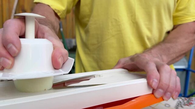 Man using manual mandoline slicer with holder to slice radish into bowl outdoors.