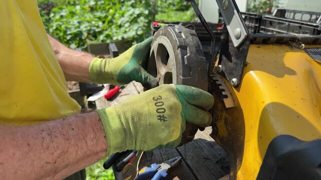 Worker attaching wheel back onto lawn mower body during summer garden work.