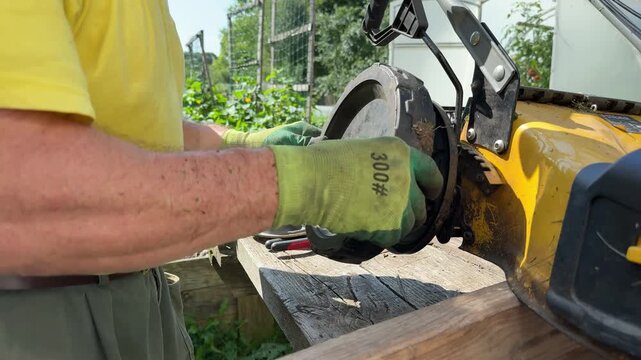 Close up of gardener hands replacing broken wheel on yellow lawn mower.