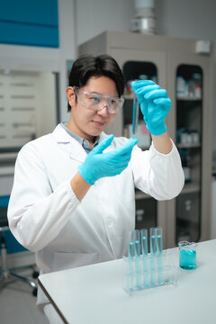 Young Asian male researcher examines test tube sample while wearing safety goggles in modern laboratory
