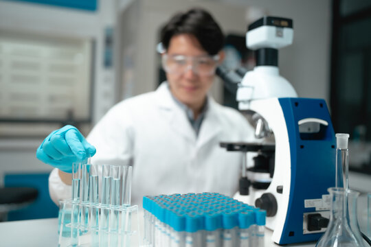 Asian scientist holding test tube rack while examining samples near microscope in laboratory setting