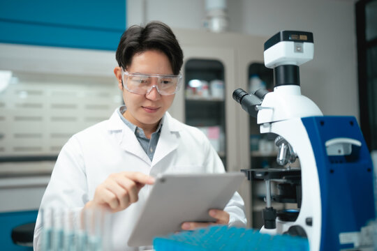 Young Asian scientist reviewing data on tablet beside microscope in modern laboratory setting