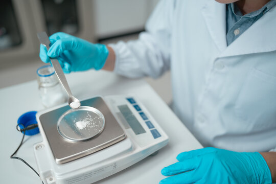 Scientist weighing white powder sample on precision scale using tweezers in laboratory setting