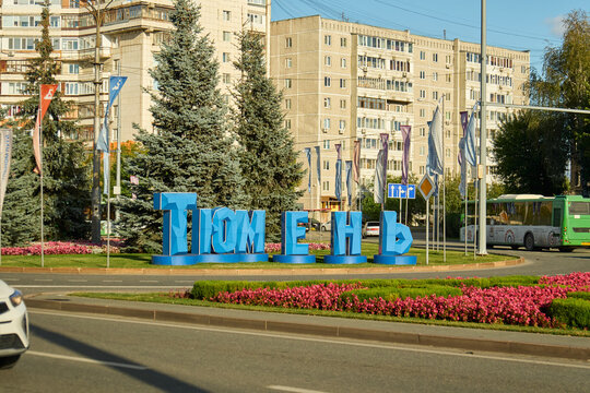 Tyumen, Russia - September 6, 2026: Large blue letters spelling Tyumen installed on flowerbed roundabout with passing city bus and residential buildings