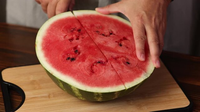 Woman slices half a watermelon into slices on a wooden board