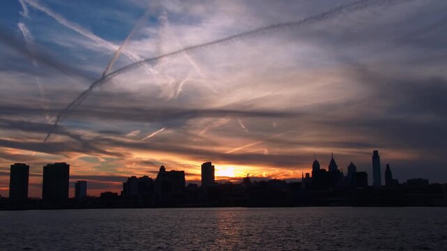 Stunning sunset over the philadelphia skyline with colorful clouds and contrails reflecting on the delaware river.