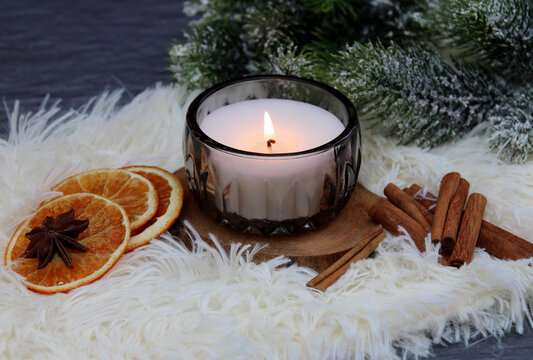 Scented candle in a glass with cinnamon, dried oranges, and star anise.
