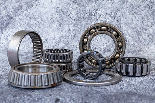 Assorted steel roller and ball bearings arranged on textured concrete workshop floor.