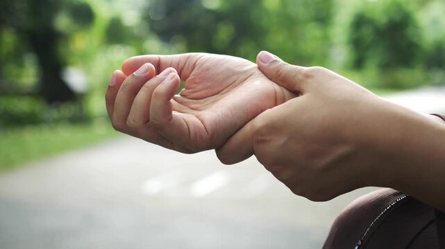 Woman suffering from wrist pain massaging sore joint outdoors in garden during day