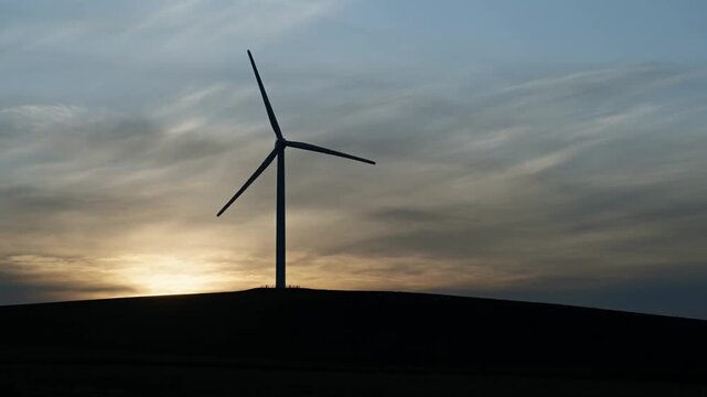 Wind turbine standing on a dark hill against a cloudy sunset sky