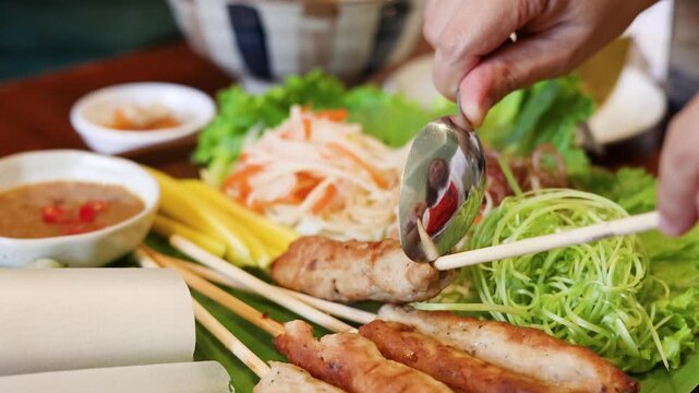 Person prepares fresh Vietnamese spring rolls with grilled pork and vegetables for wrapping.