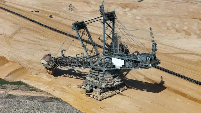 bucket wheel excavator works beside conveyor belt bridge terraced lignite pit sand walls steel lattice boom cables drone aerial view hambach coal mine germany surface mining heavy machinery extraction
