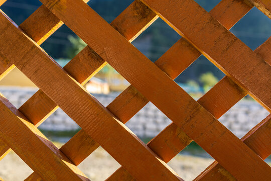 Wooden lattice fence with diagonal criss cross slats in bright natural sunlight, traditional timber trellis woodwork with geometric diamond patterns and soft bokeh