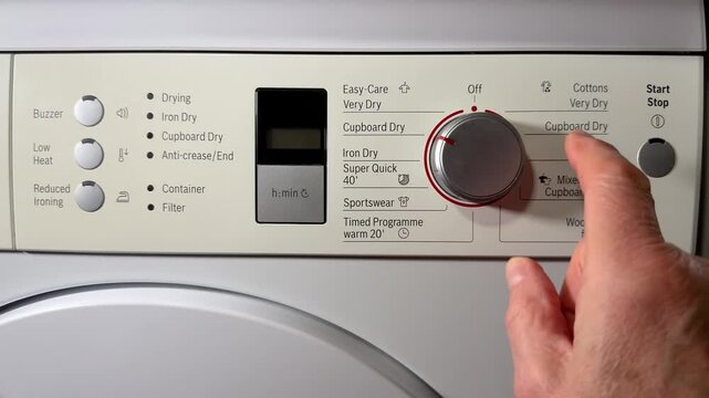 Closeup of a man&rsquo;s hand turning the selector control knob on a tumble dryer, then pressing the start button to activate the clothes drying program.