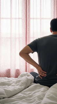 Man with back pain holding his lower back while sitting on a rumpled bed, symbolizing discomfort and pain. free space