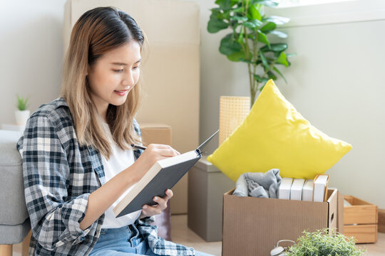 Move house, relocation. Woman write down and draw renovate room on notebook for new apartment, Inside the room are cardboard boxes containing personal belongings and furniture. Move into a house.
