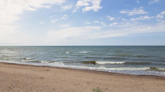 Sandy beach with waves rolling ashore under blue sky