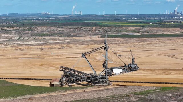 colossal bucket wheel excavator works lignite pit twin cooling towers steam beyond wind turbines farmland patchwork horizon drone aerial establishing shot hambach coal mine germany infrastructure