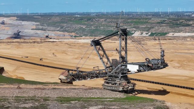 bucket wheel excavator works terraced lignite pit second excavator visible distant level wind turbines span horizon small town borders mine edge drone aerial orbit hambach coal mine germany mining