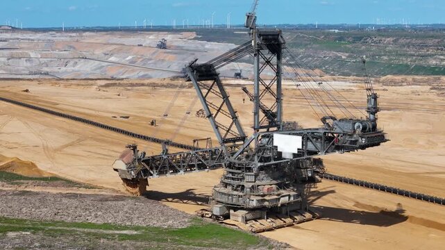 massive bucket wheel excavator towers over hambach lignite mine terraced open pit stretches toward horizon wind turbines line distant ridge conveyor belts cut through golden earth kerpen germany