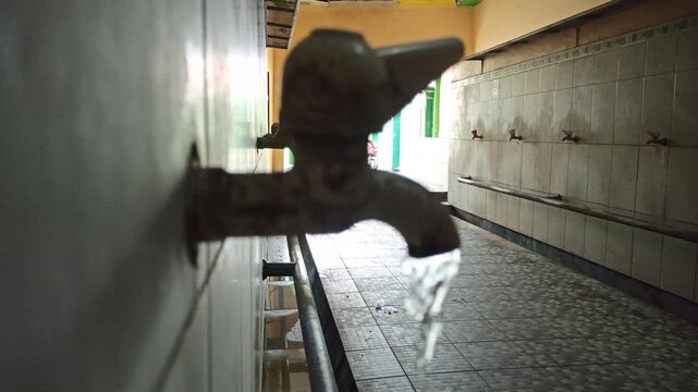 Wall-mounted water faucet with clear water flowing continuously, showcasing a simple household plumbing fixture for bathroom, kitchen, utility area, and water conservation concepts
